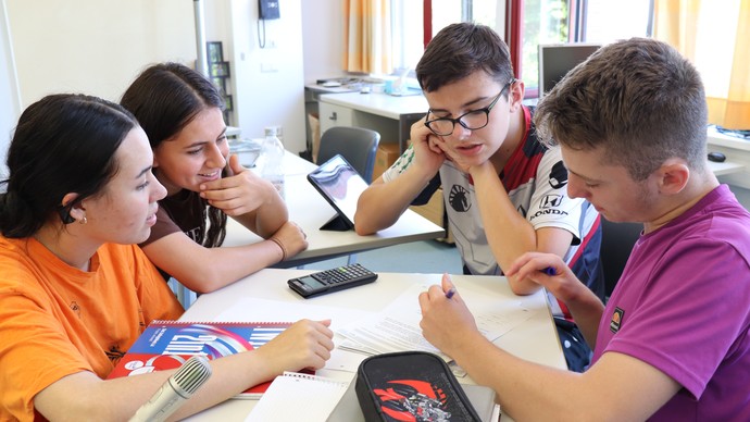 Schüler:innen sitzen zu viert zusammen und bearbeiten eine Aufgabe.