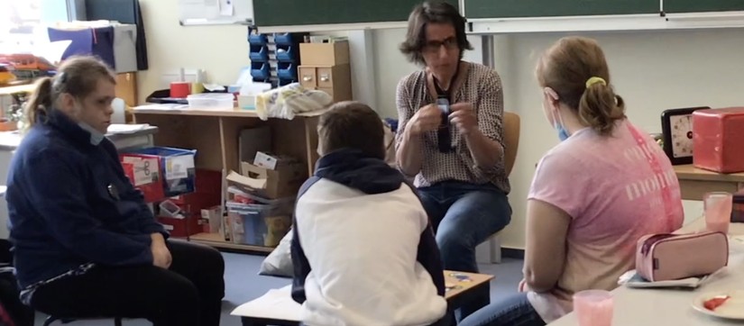 Drei Schüler:innen sitzen im Kreis mit ihrer Lehrerin und unterhalten sich. Die Lehrerin kommuniziert in Gebärdensprache mit einer Schülerin.