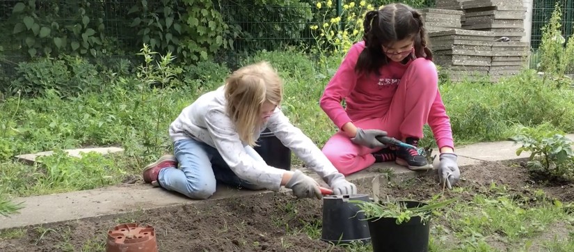 Zwei Mädchen sitzen an einem Gemüsebeet und pflanzen etwas ein