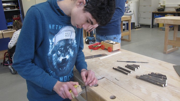 Ein Junge steht im Werkraum und bearbeitet ein Stück Holz